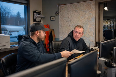 Two dispatchers reviewing a route at a desk with a wall map behind them.