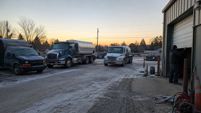 A small fuel company yard at sunrise with an oil truck, a propane truck, and a service van.